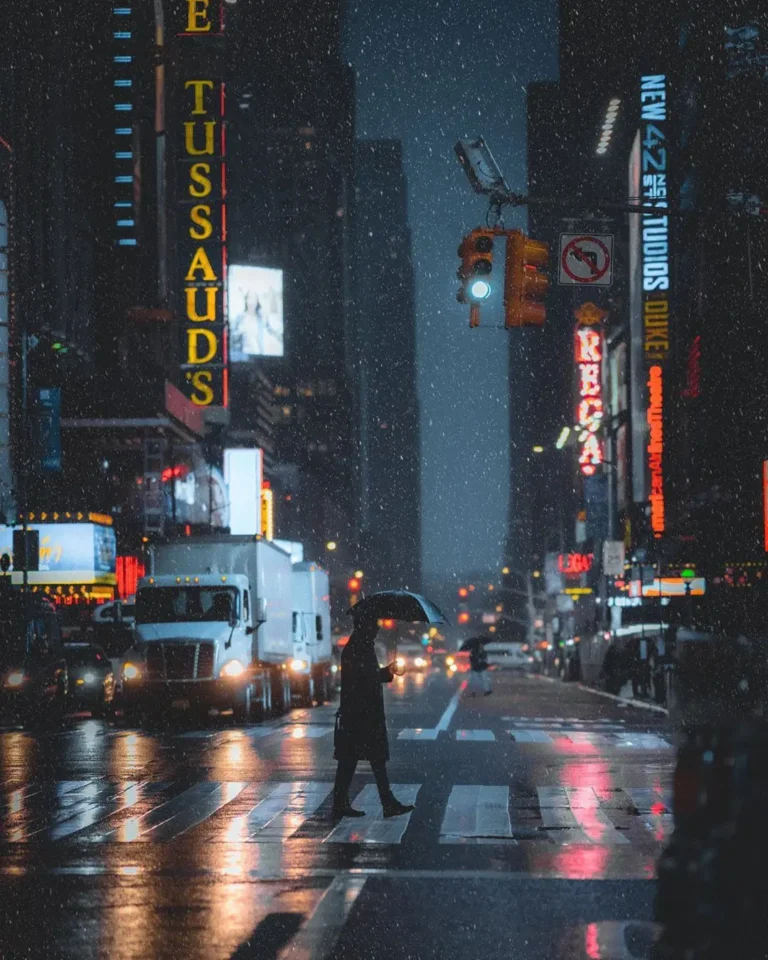 Fotografía de Nicolas Miller en Times Square, Nueva York, con neón, lluvia y figura con paraguas cruzando la calle.
