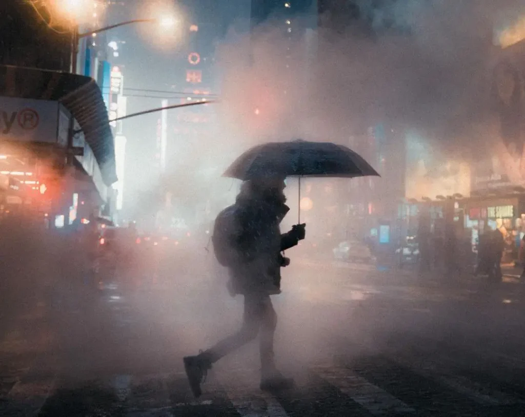Fotografía de Nicolas Miller en Times Square, Nueva York, con niebla, luces urbanas y una figura con paraguas.