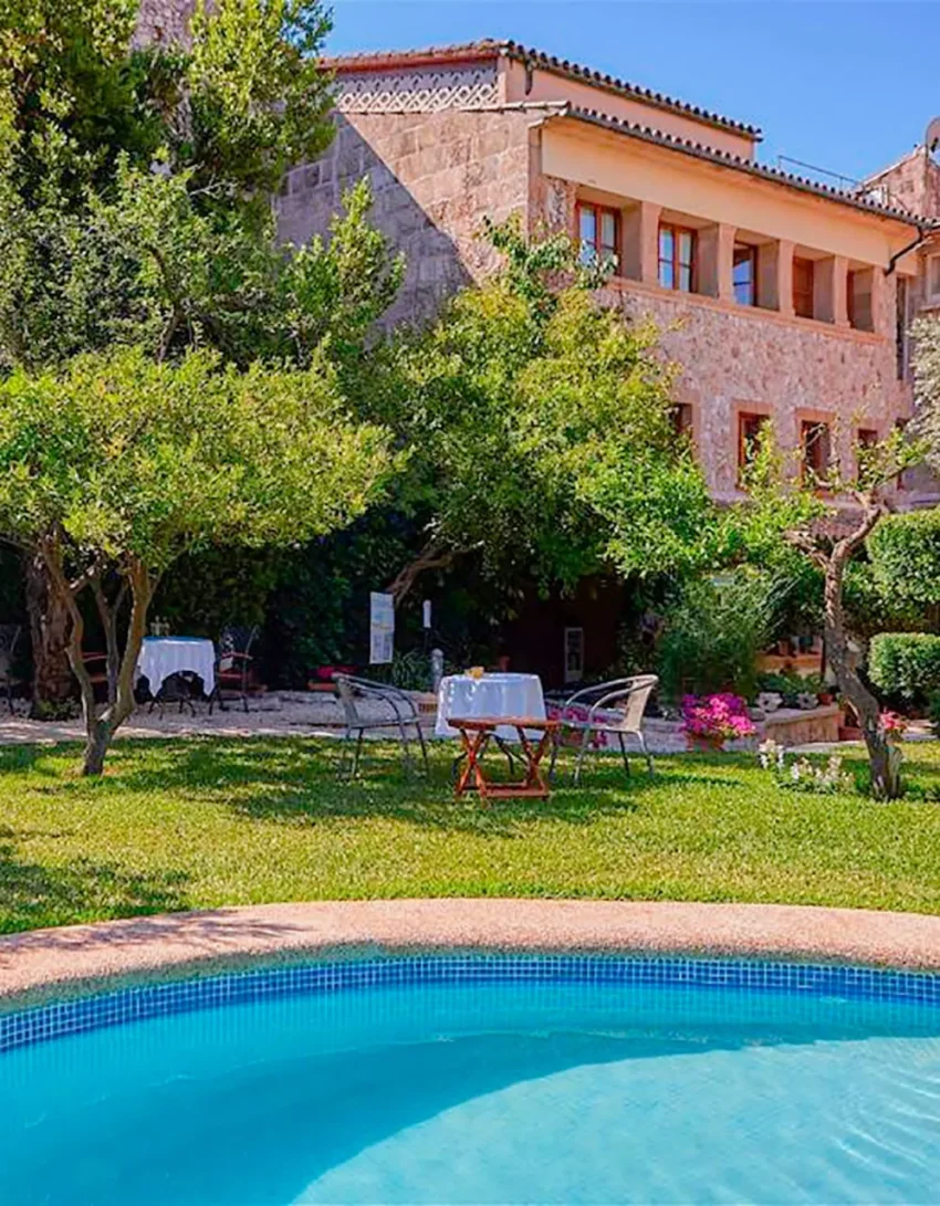 Jardín mediterráneo con piscina y mesas bajo árboles centenarios en Son Sant Jordi, Pollença