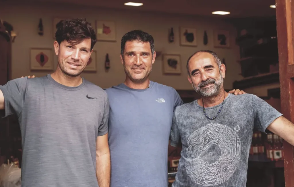 Tres personas sonrientes posan en interior de tienda con botellas y cuadros en la pared