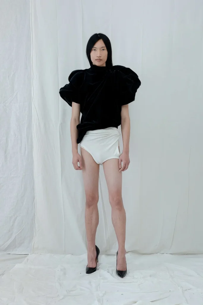 Modelo con look de Antonio Acuario: blazer estructurado, suéter gris y falda asimétrica sobre pantalón, frente a fondo claro.