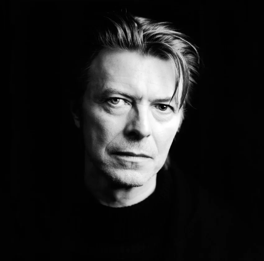Retrato en blanco y negro de David Bowie con expresión neutra y fondo oscuro