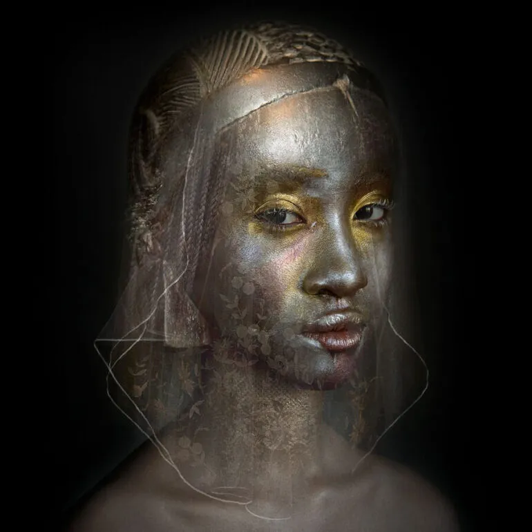 Retrato artístico de mujer negra con velo translúcido, maquillaje metálico y peinado escultórico sobre fondo oscuro