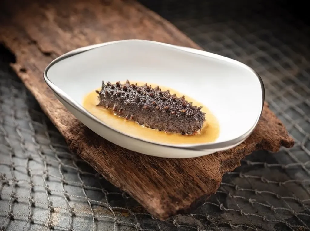 Pepino de mar servido en salsa ligera sobre bol blanco, plato insignia del chef Vicky Cheng en Wing_HongKong.