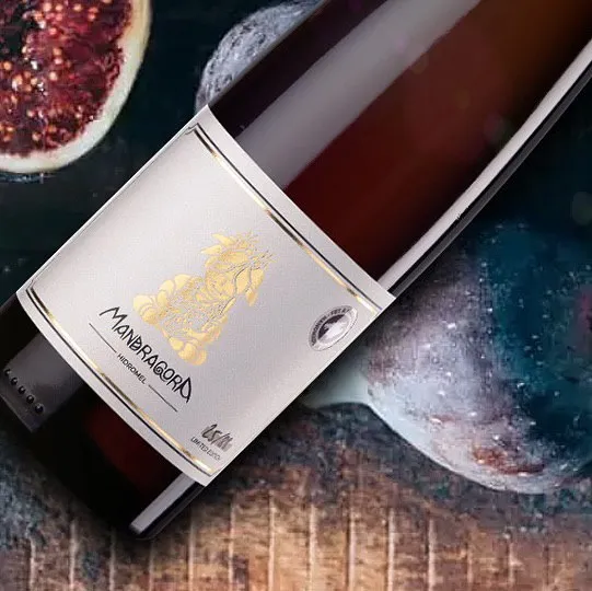 Botella de hidromiel Mandragora con ilustración dorada de raíz mágica, acompañada de higos sobre madera rústica.