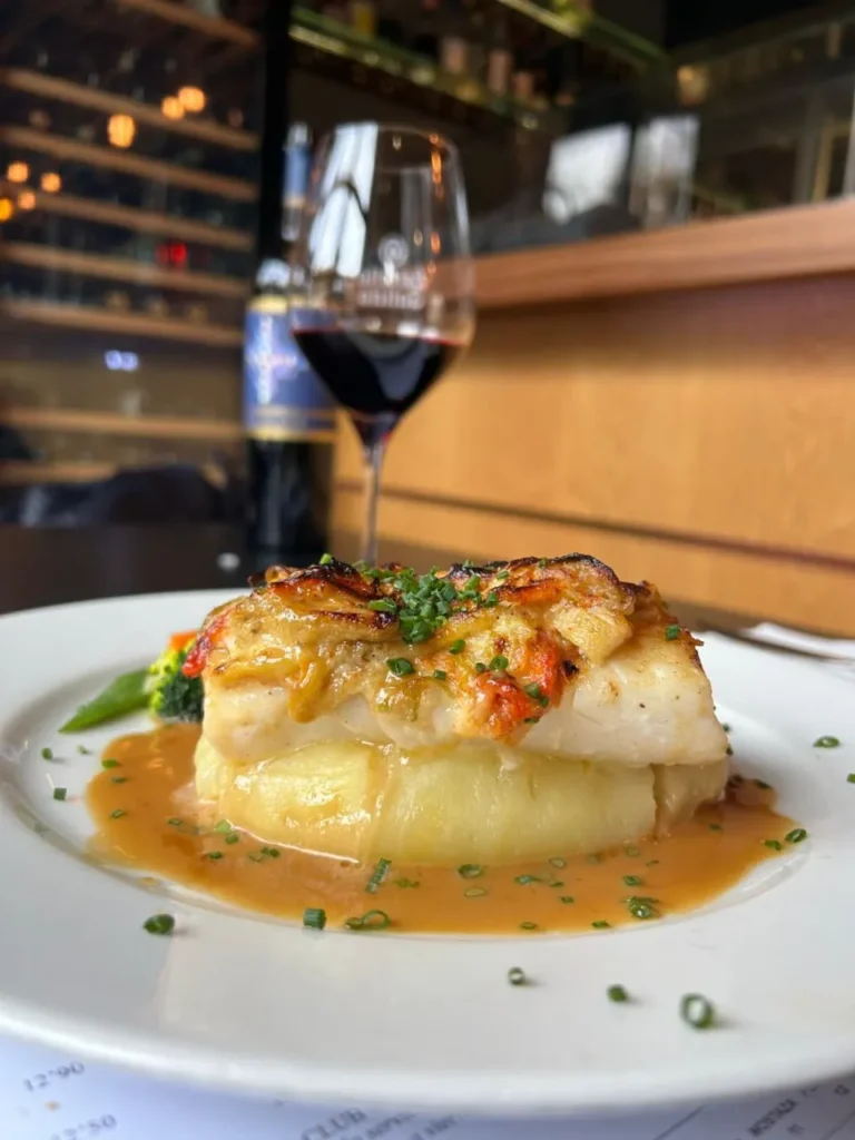 Bacalao en crosta sobre crema de patata, acompañado de salsa y vino tinto en restaurante S’Àngel.