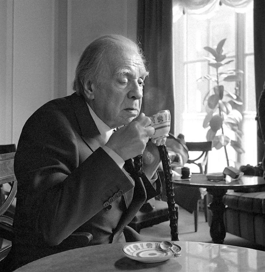 Jorge Luis Borges sosteniendo una taza de té en una escena interior, fotografía en blanco y negro