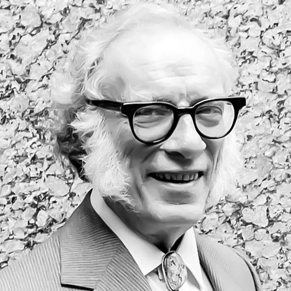 Retrato en blanco y negro de un hombre mayor con gafas, patillas gruesas y traje con corbata bolo frente a una pared de piedra