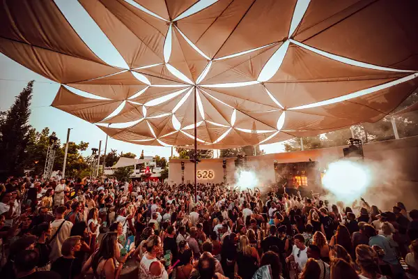 Multitud disfrutando un concierto al atardecer bajo una estructura geométrica en 528 Ibiza.