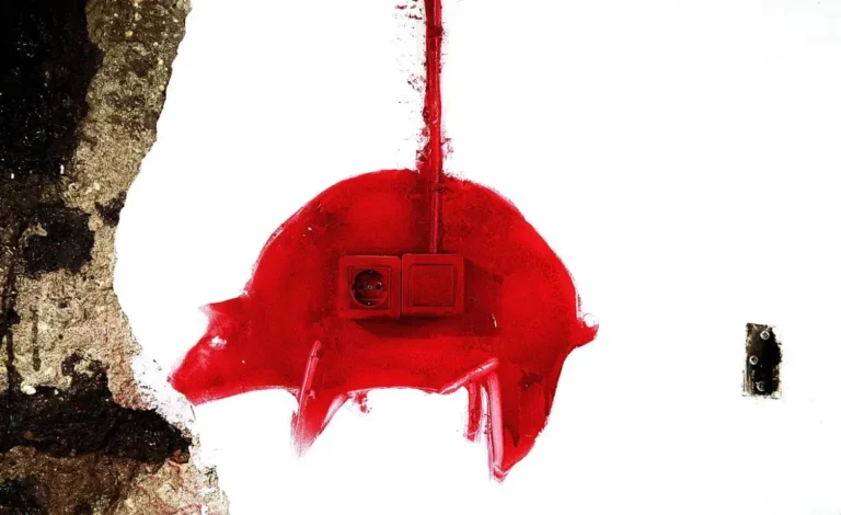 Intervención artística en una pared donde dos enchufes y pintura roja forman la silueta de un cerdito, en una escena comentada por Carlos Penas.