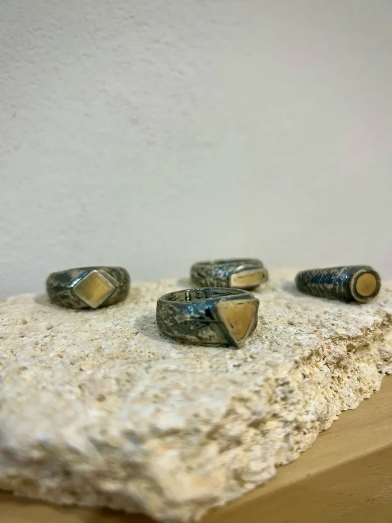 Anillos artesanales de Rako Joies con formas geométricas sobre una piedra texturizada.