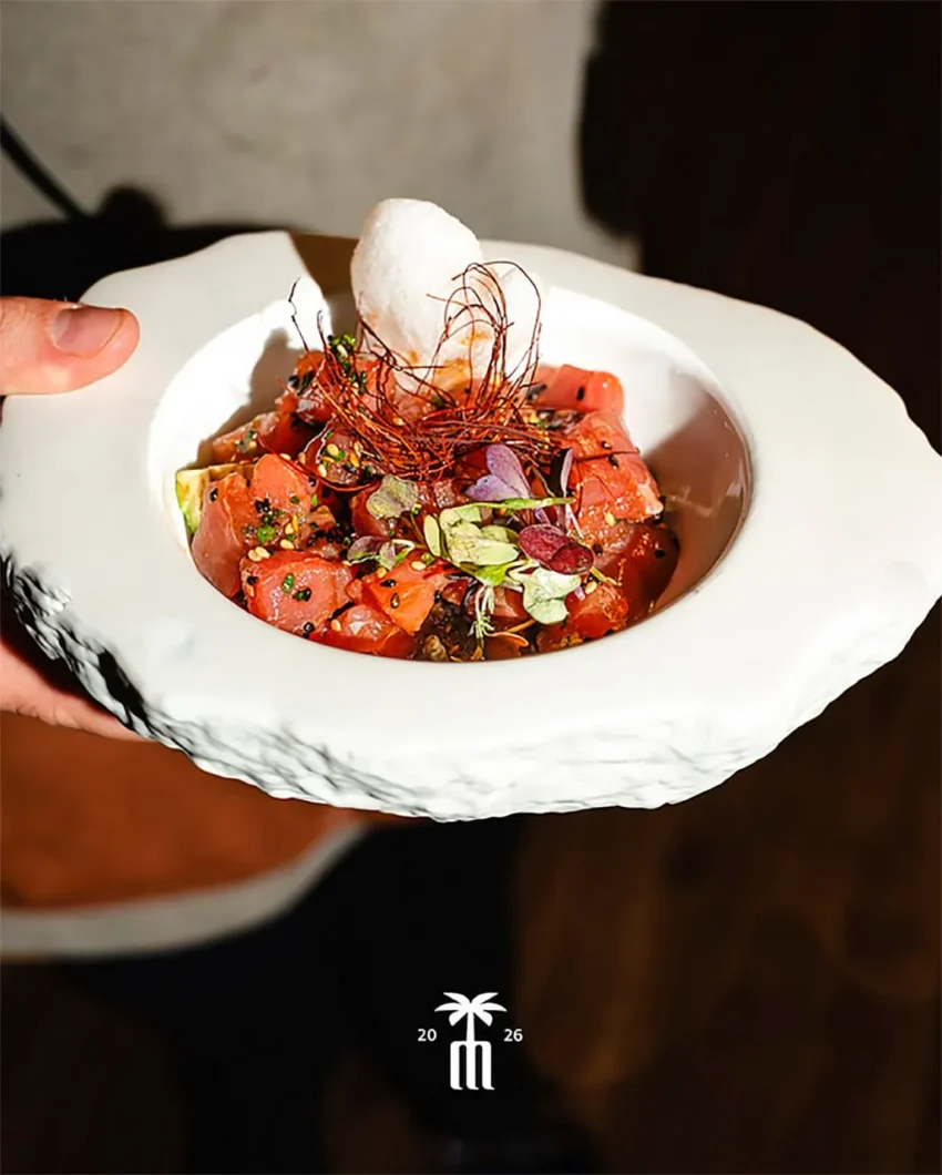 Plato gourmet con atún marinado, brotes y crujiente blanco servido en un cuenco cerámico artesanal.