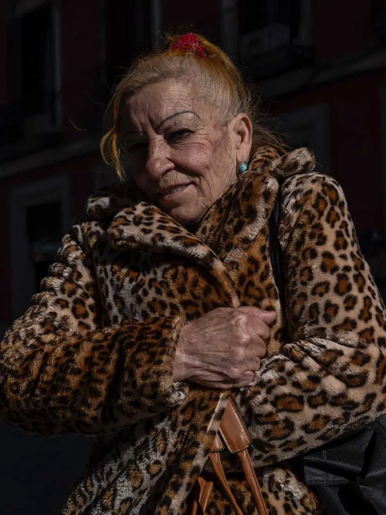 Primer plano de una mujer mayor sonriendo levemente, vistiendo un abrigo con estampado de leopardo bajo una luz solar intensa que resalta las texturas de su piel y el tejido.