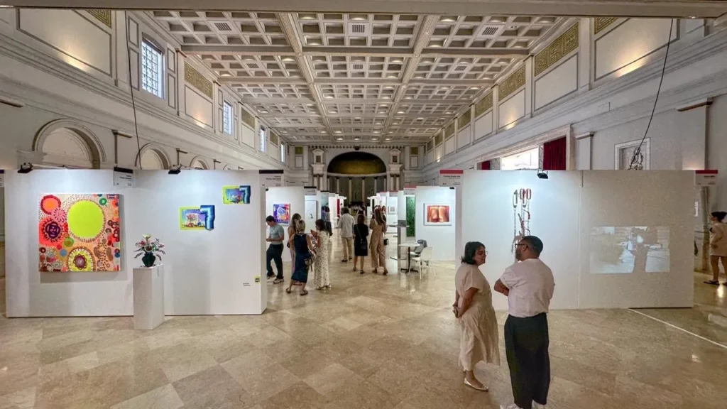 Visitantes recorren una galería de arte con techos altos y obras contemporáneas expuestas en paneles blancos.