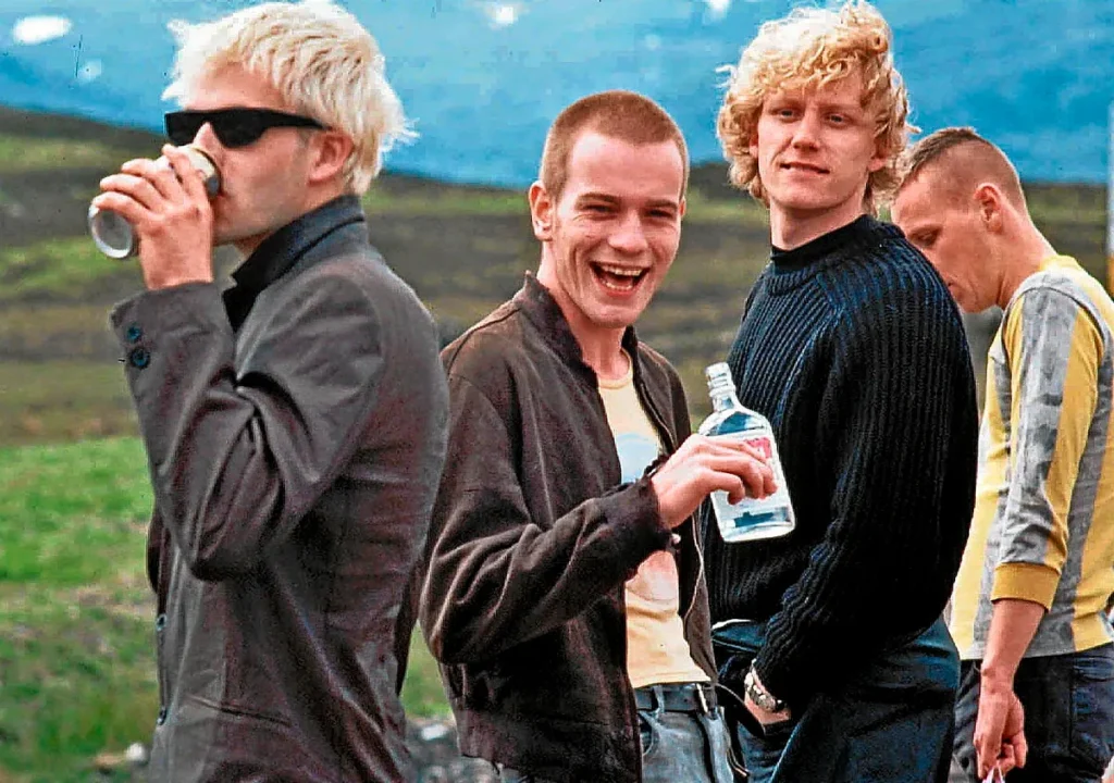 “Fotograma de Trainspotting con cuatro personajes en un paisaje escocés, posando con actitud despreocupada.”