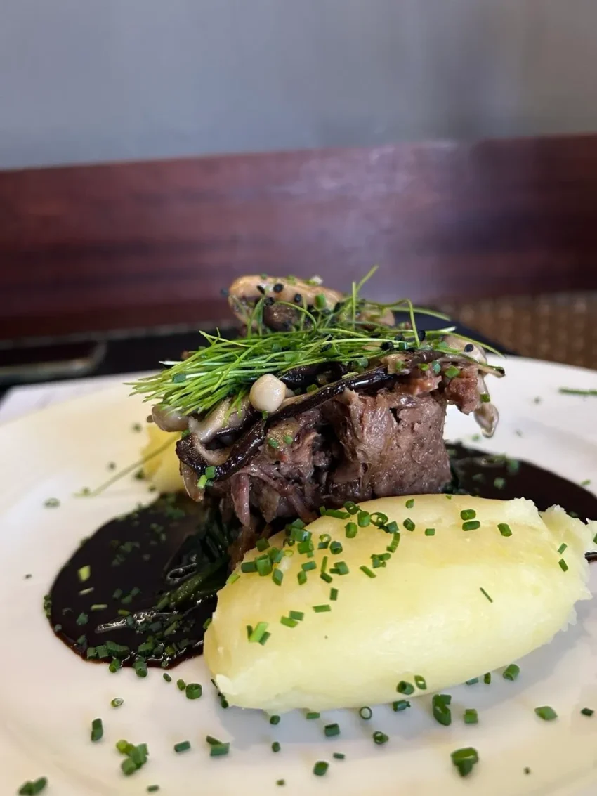 Rabo de toro deshuesado con setas, salsa de vino tinto y puré de patatas con cebollino fresco.