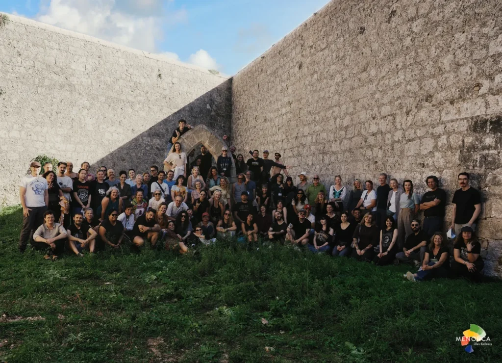 “Participantes de Quarantine Menorca reunidos entre muros de piedra en la isla de Lazareto para una acción colectiva.”