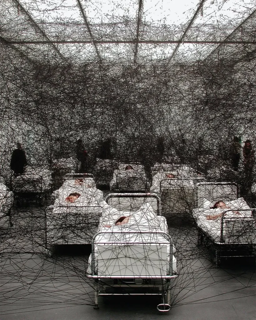 La firma distintiva de Chiharu Shiota son sus instalaciones con hilos de lana, principalmente en colores rojo intenso y negro. Estos elementos no son meros componentes decorativos, sino verdaderas metáforas visuales que conectan