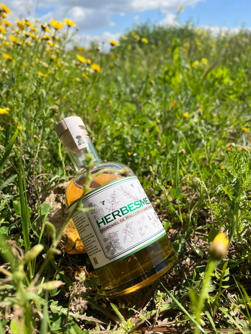 Botella de Herbesme Hidromel de Mallorca entre hierba y flores silvestres al aire libre